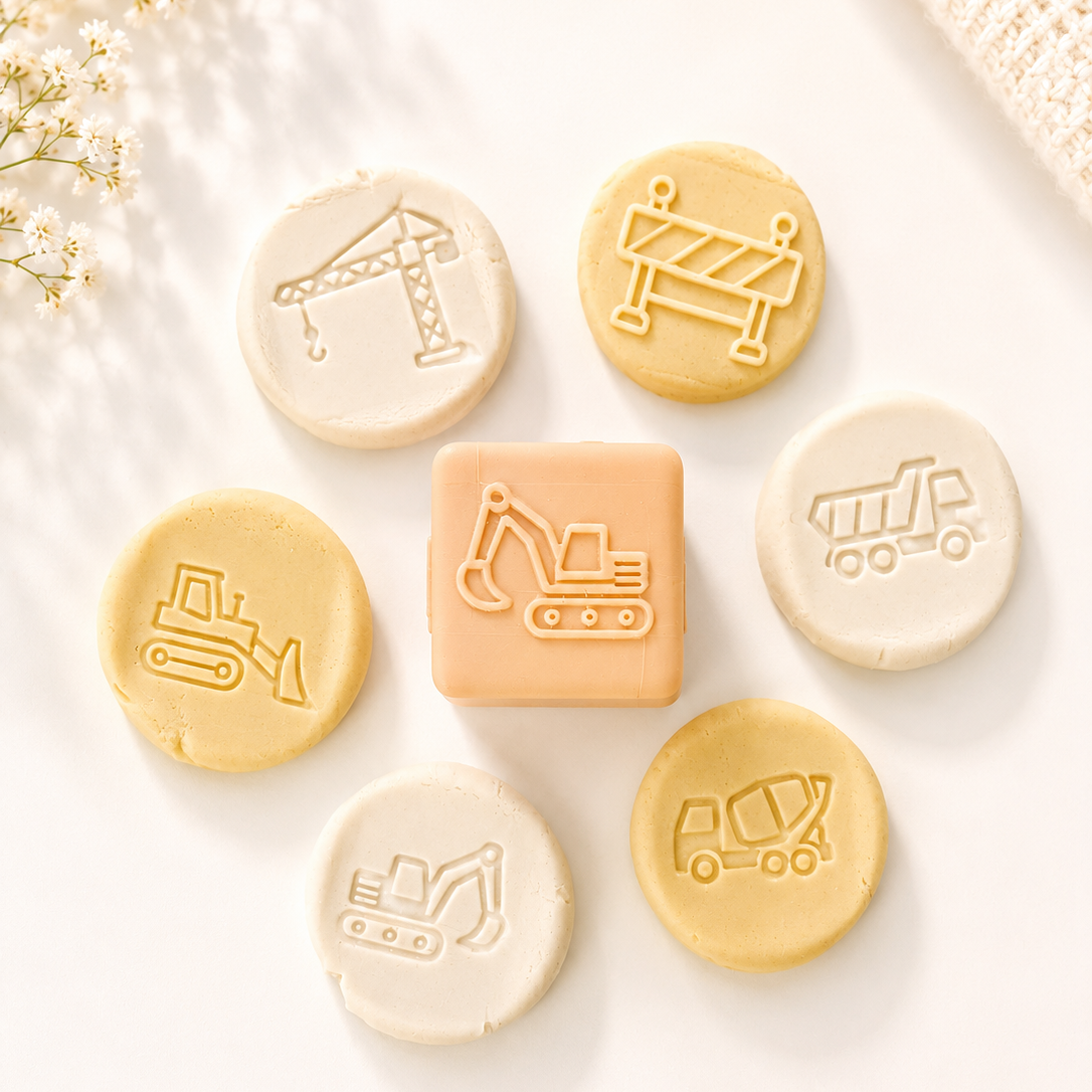 A set of construction-themed baby teethers or bath toys arranged on a white surface. The set includes a central square piece with an embossed excavator, surrounded by six round pieces with embossed construction icons: a crane, a barrier, a bulldozer, a dump truck, a excavator, and a dump truck.